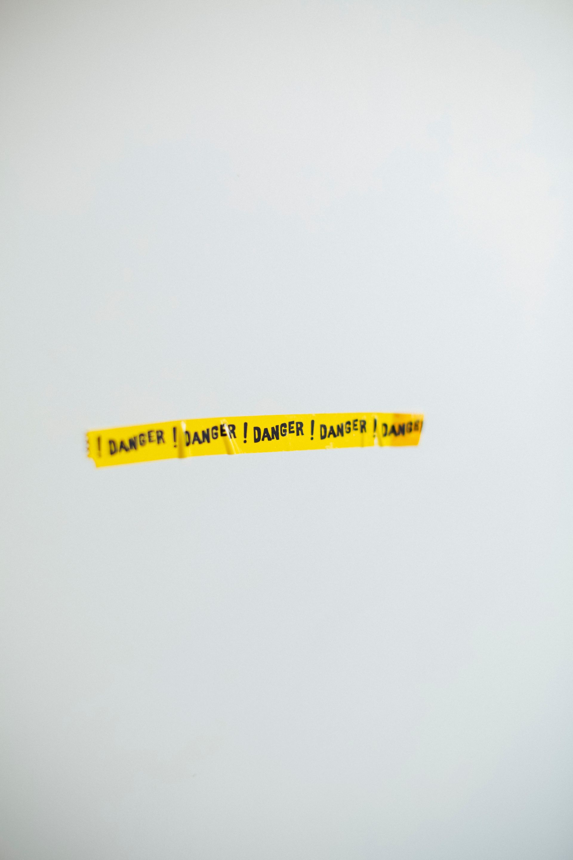 A strip of yellow danger tape against a plain gray wall, conveying caution