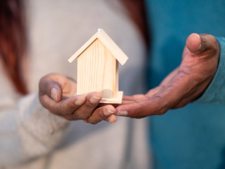 Close-up of hands holding a miniature wooden house symbolizing home ownership