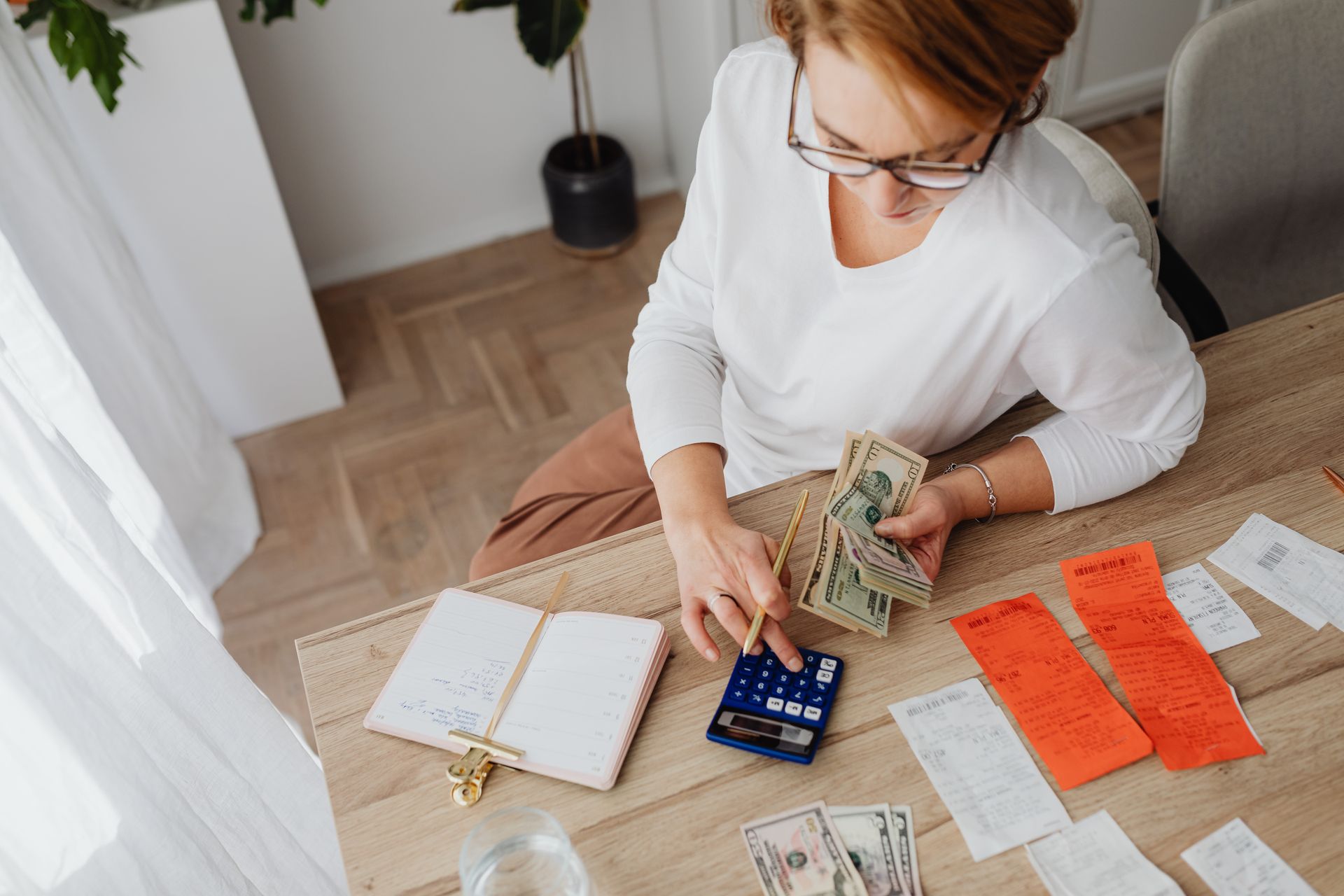 Woman computing expenses while holding dollar bills