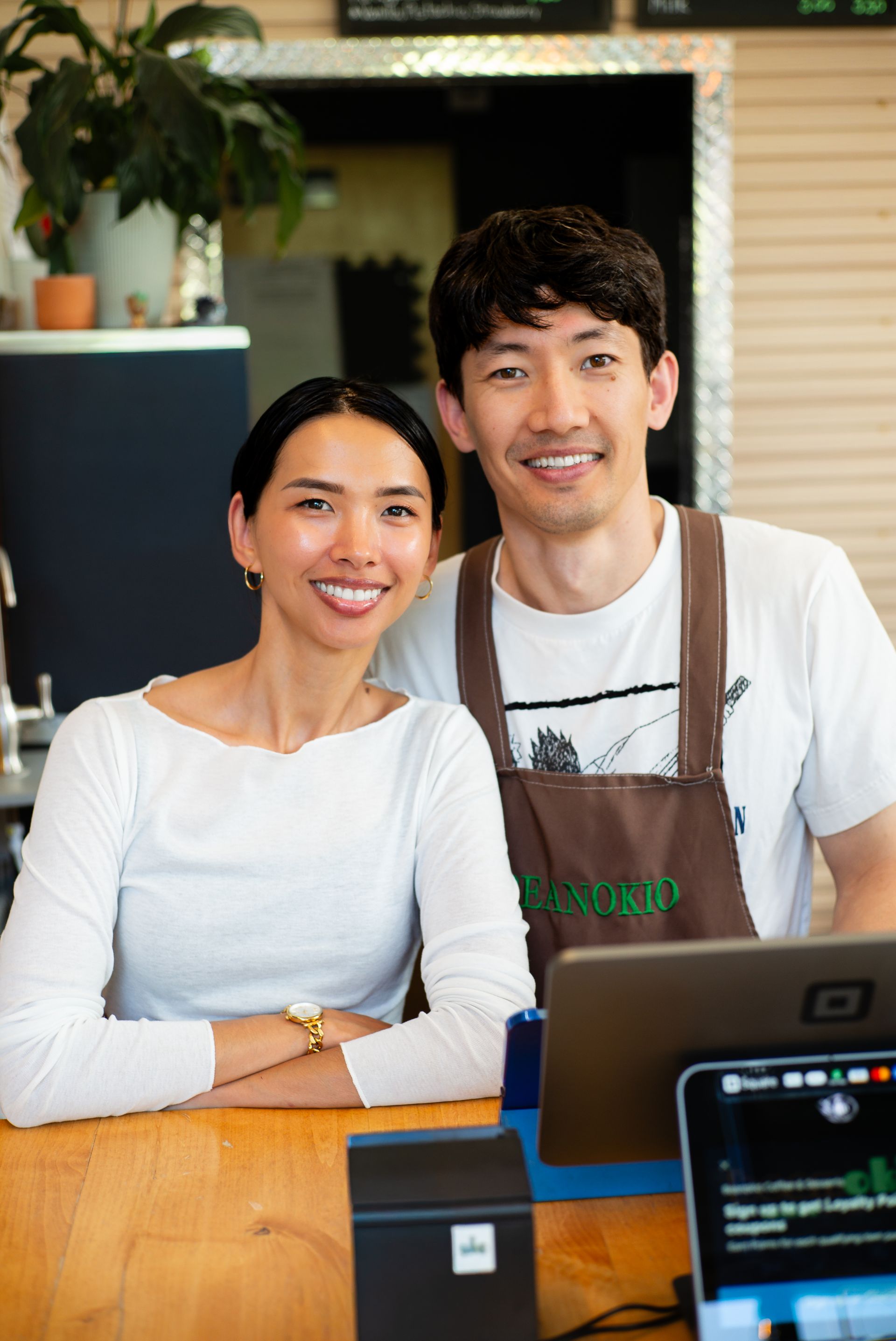 Two smiling small business owners standing behind their coffee shop counter