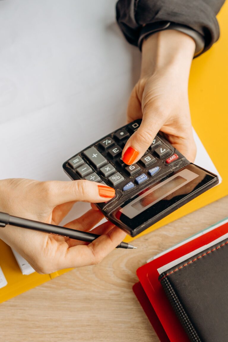 Hands using a calculator on a desk surrounded by stationery