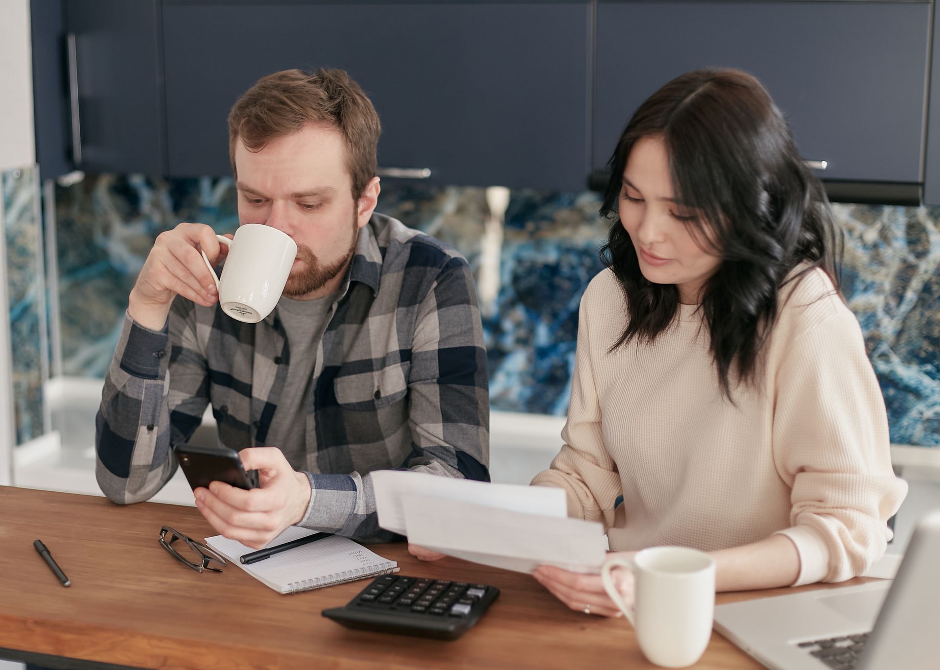 Couple reviewing bills with a calculator and smartphone in the kitchen