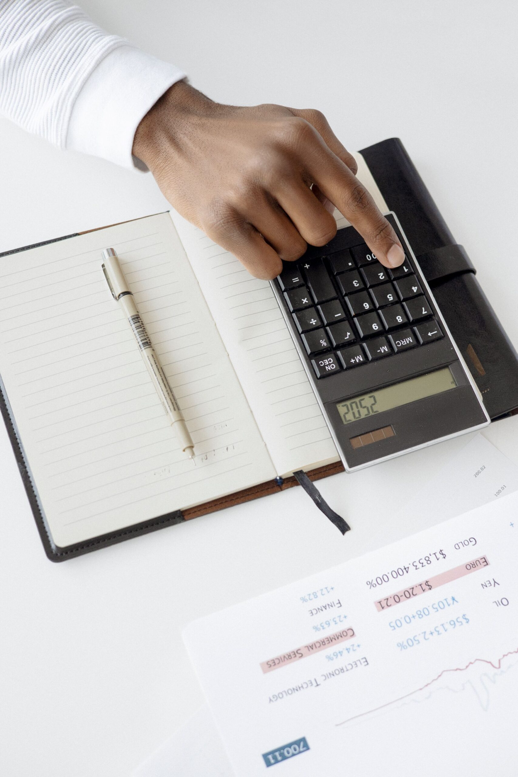 Hand using a calculator with financial documents and notebook