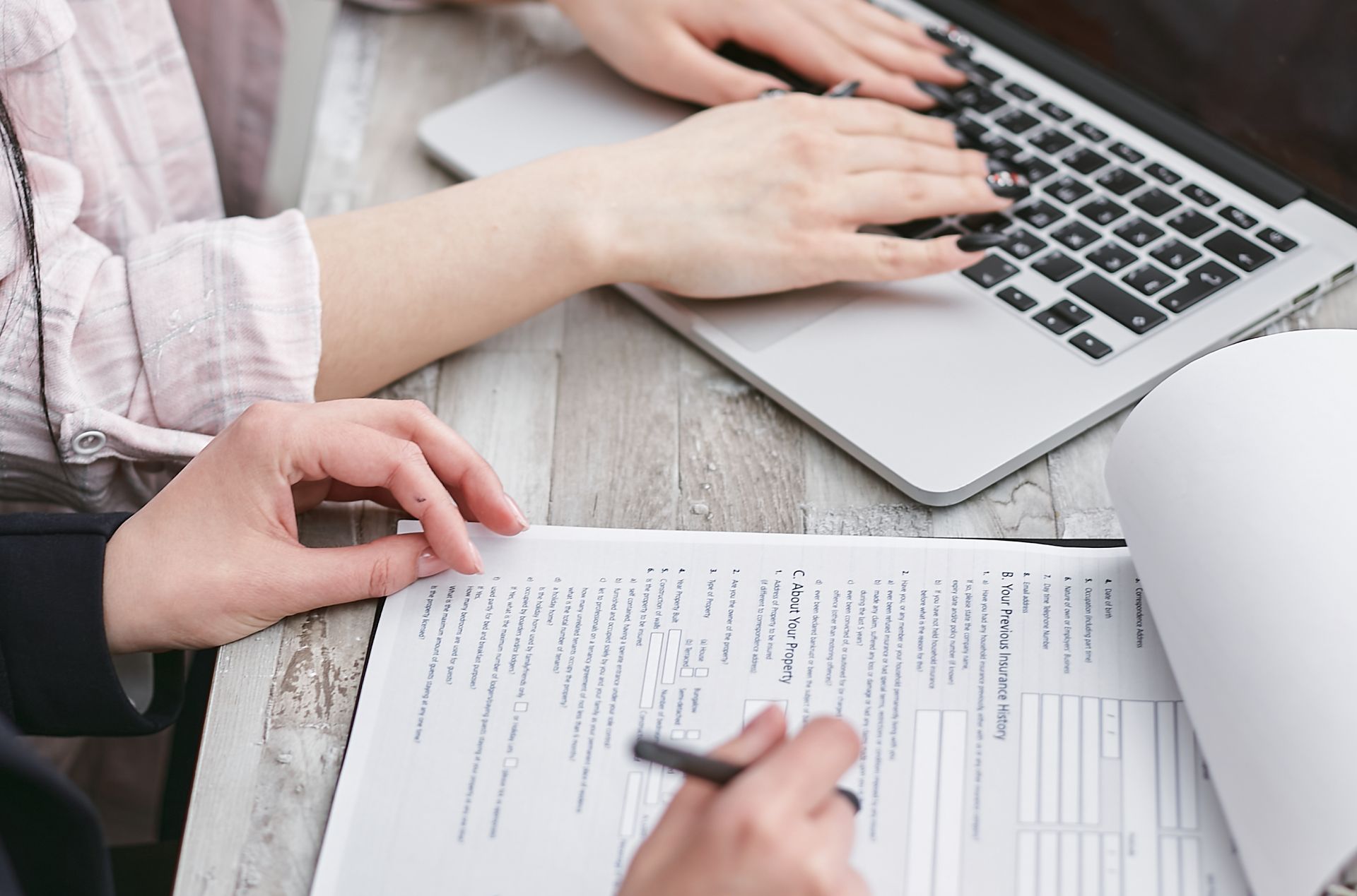 Hands typing on a laptop while reviewing business documents