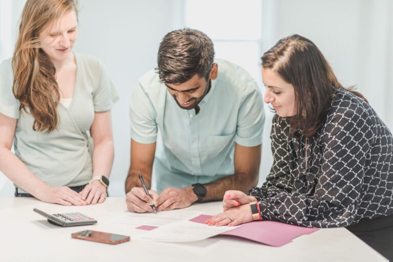 Three adults reviewing and signing loan documents indoors