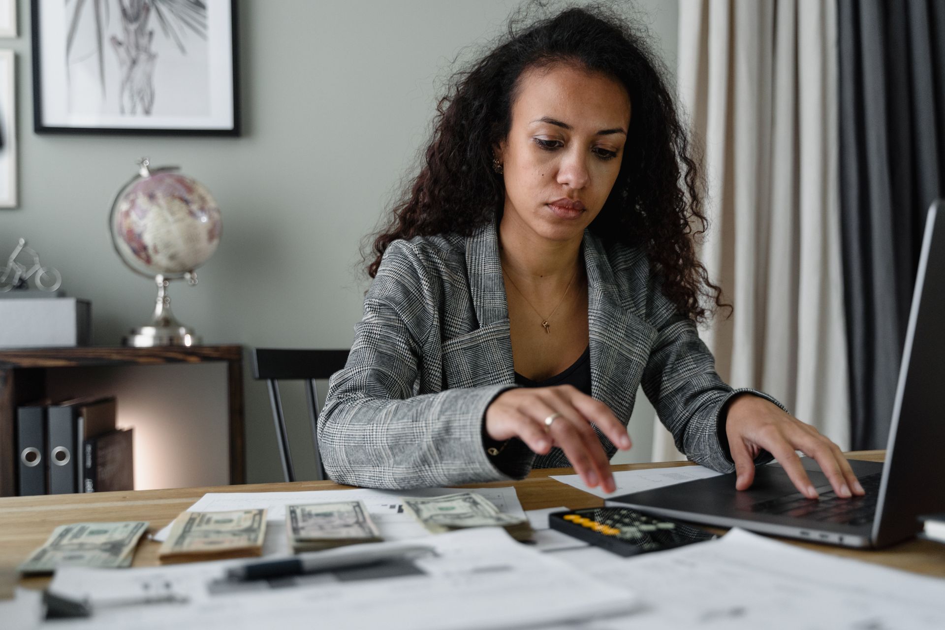 Woman in a plaid blazer using a laptop and mobile phone to manage finances