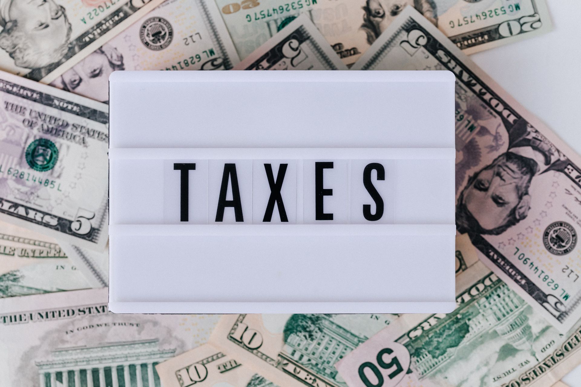 Stack of dollar bills with a taxes lightbox, a reminder that every balance has a cost