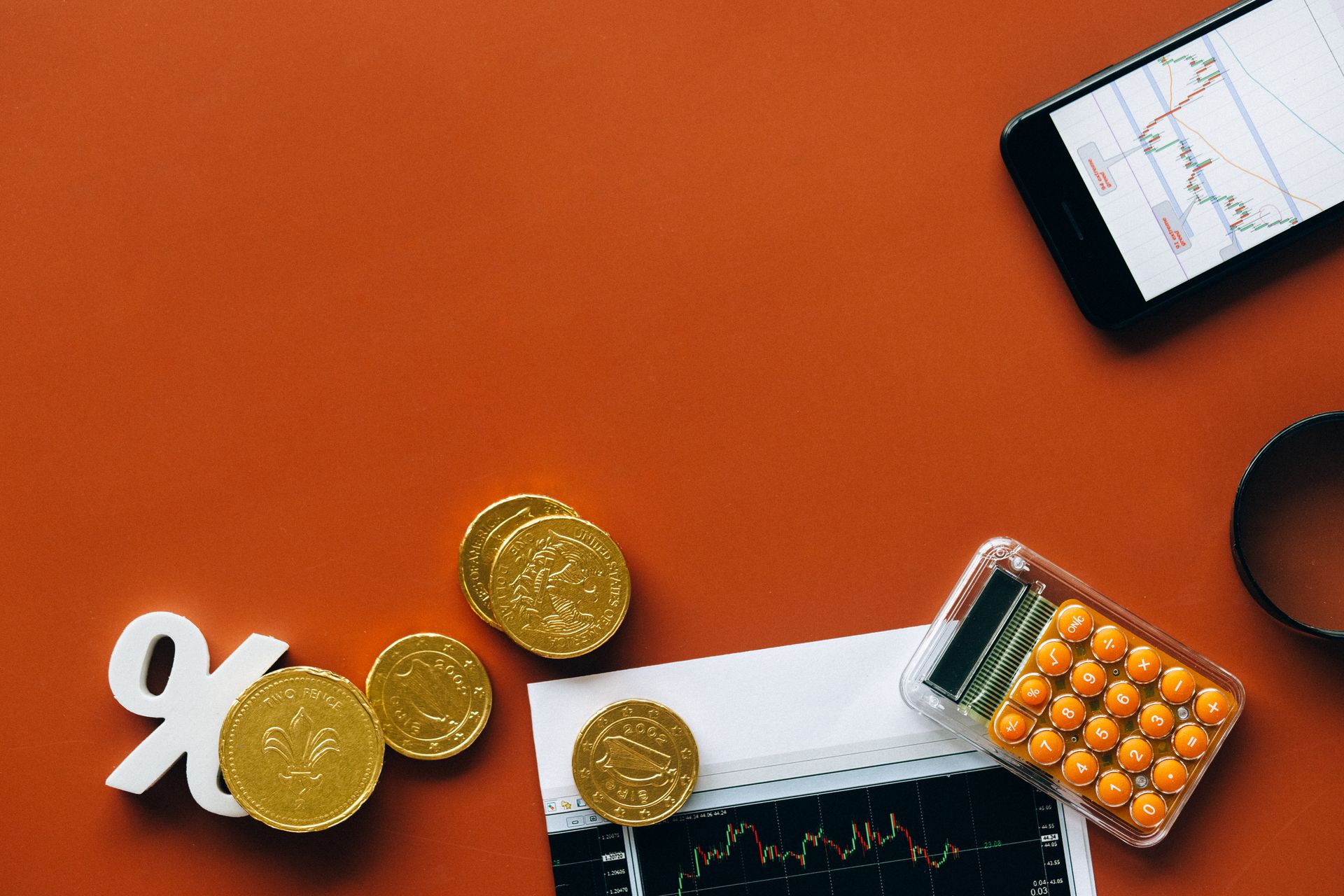 Flat lay of coins, calculator, and charts on a red background for financial analysis