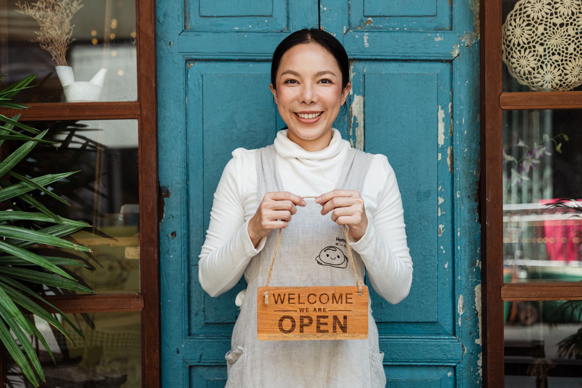 Small business owner holding a welcome we are open sign at her cafe entrance