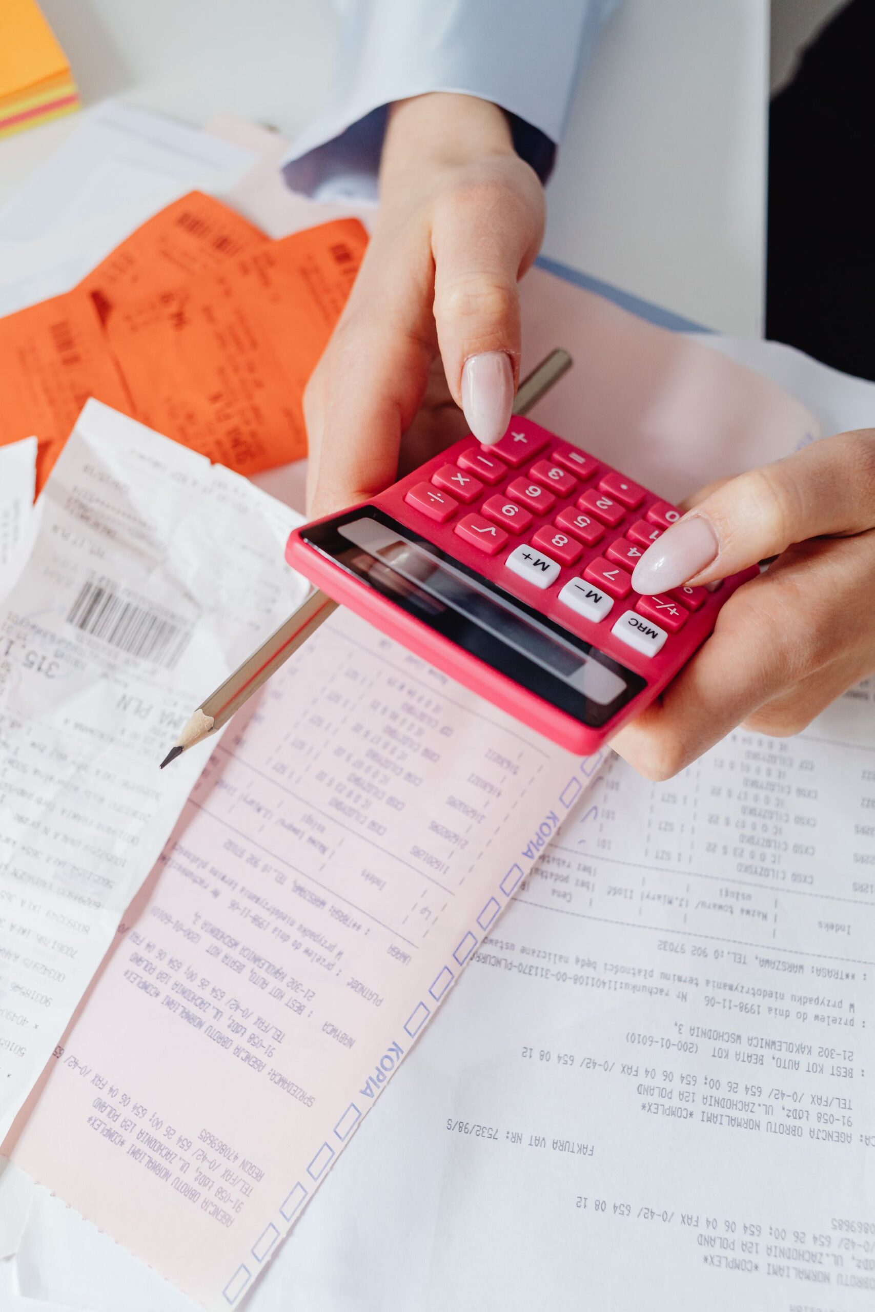 Hands using a red calculator surrounded by financial documents and receipts
