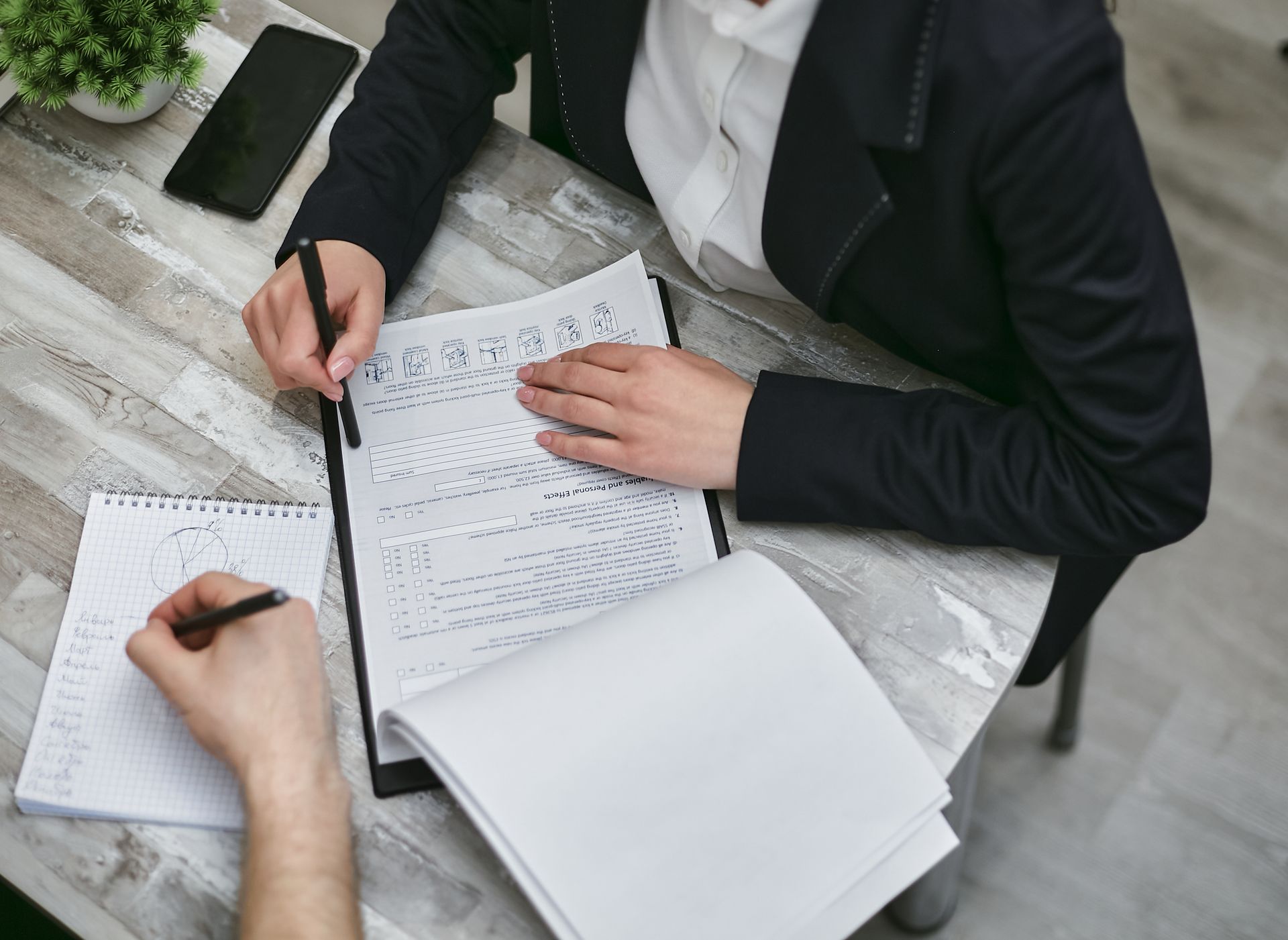 Two colleagues reviewing documents and taking notes during a business meeting