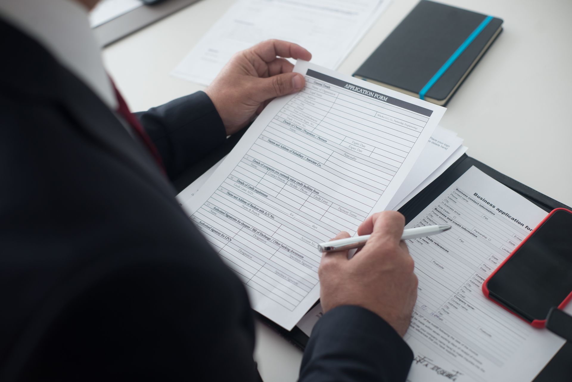 Businessman in a black suit reviewing a printed application form with a pen