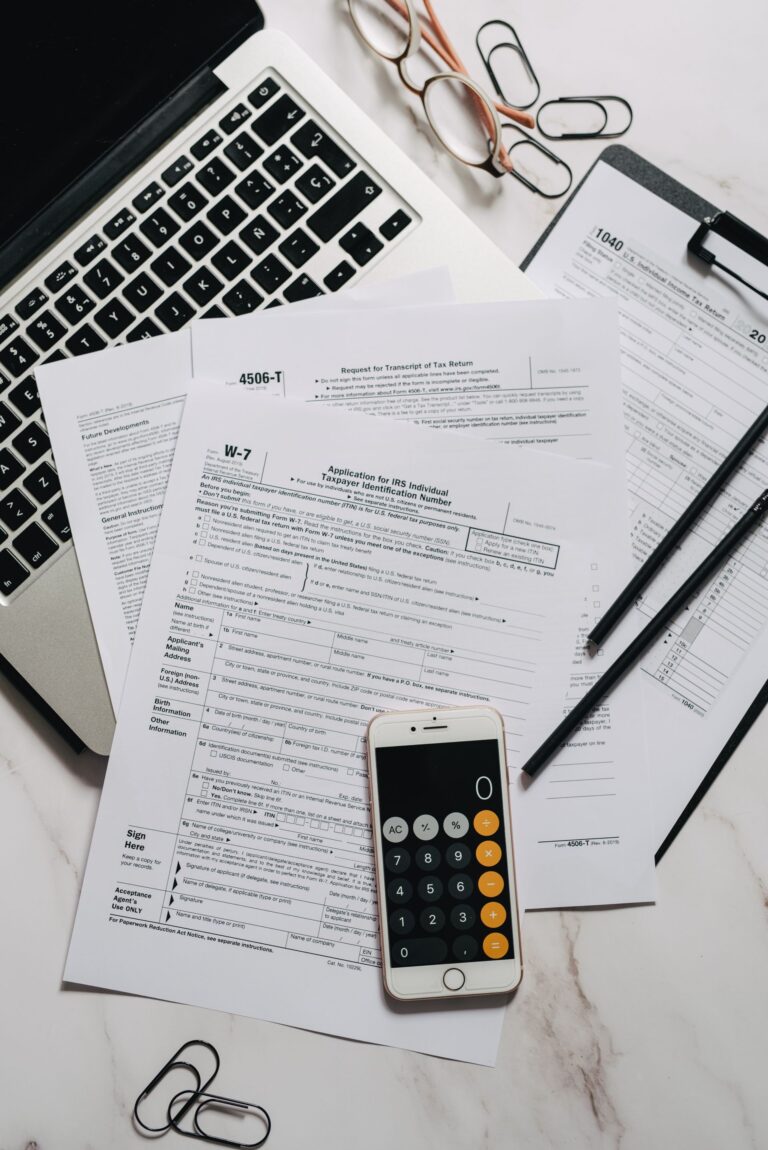 A desk with tax forms, a calculator, and a laptop for tax preparation
