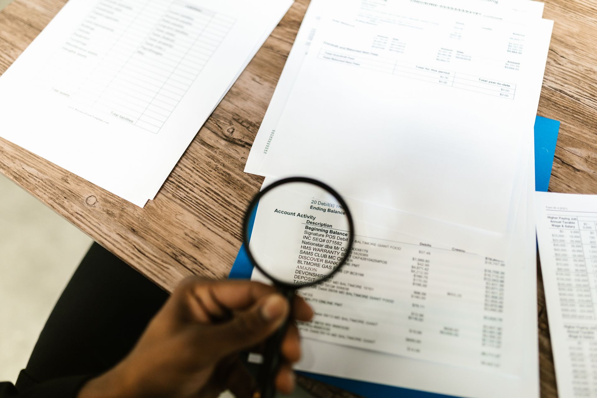 Close-up of a hand using a magnifying glass to review financial documents
