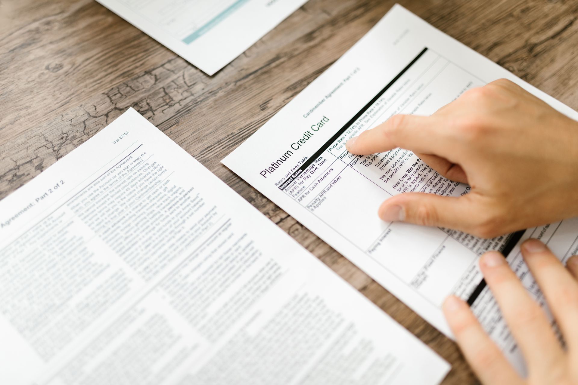 A hand examining a credit card agreement on a wooden desk