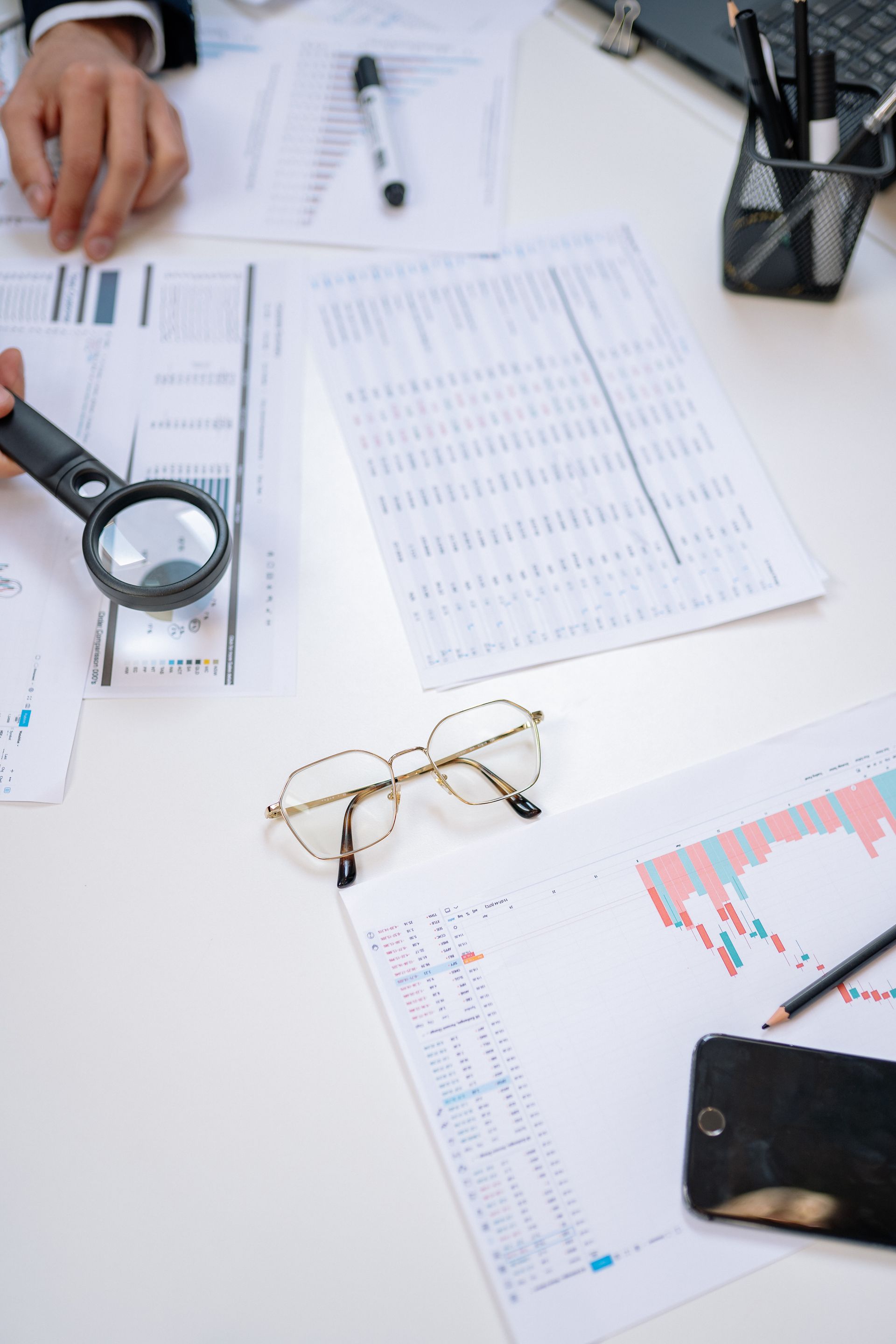 Flat lay of business documents with a magnifying glass, glasses, and smartphone on a desk